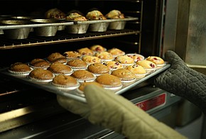 Hände mit Topfhandschuhen zieht Muffin-Blech aus dem Ofen.